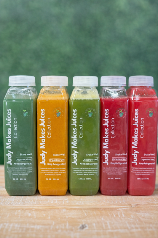 Five JMJ cold-pressed juice bottles in green, orange, and red on a wooden surface